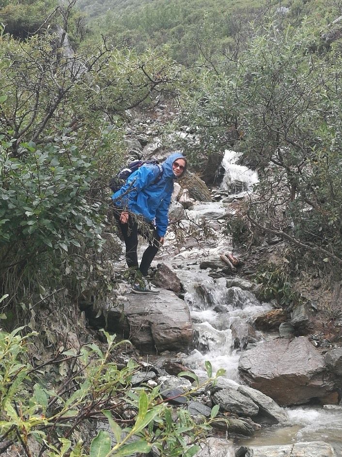 A man in a blue jacket is walking across a rocky stream.