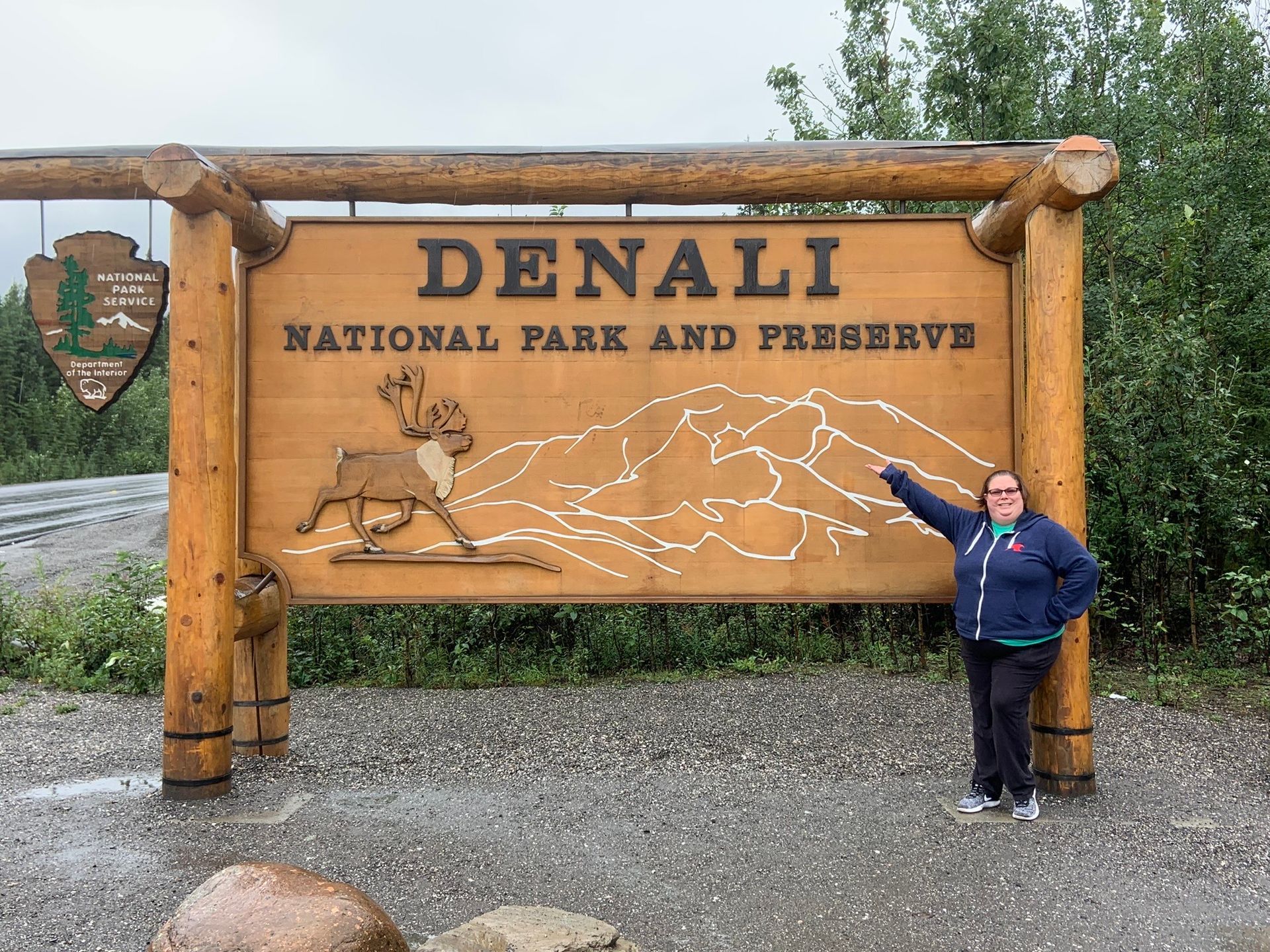 A woman is standing in front of a denali national park and preserve sign