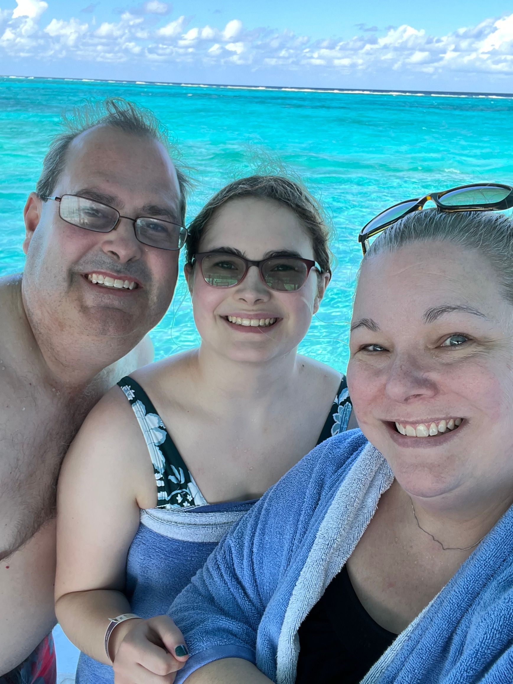 A man and two women are posing for a picture in front of the ocean.