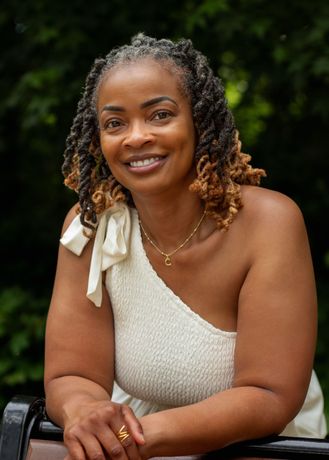 A woman with dreadlocks and glasses smiles for the camera