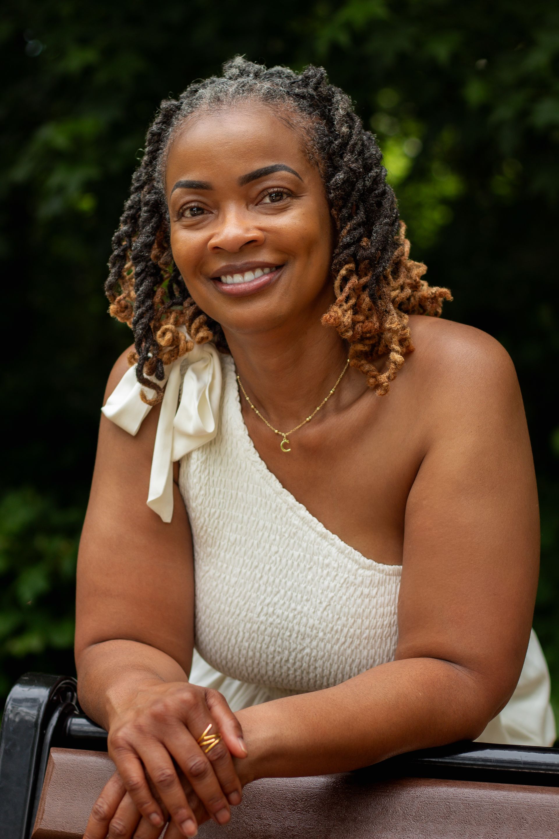 Charonda P. Gardner, African American therapist for women, smiles kindly at the camera. She has locs. She is wearing a white dress and is standing in front of trees.