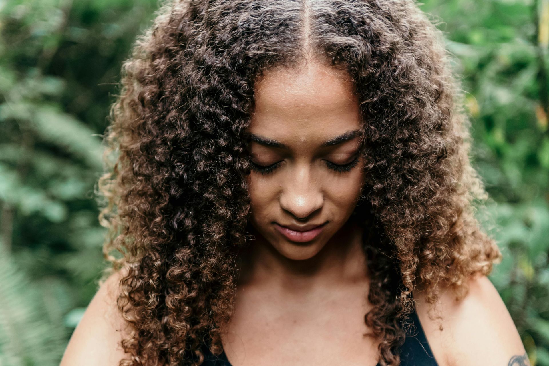 Woman with curly brown hair looking down, outdoors.