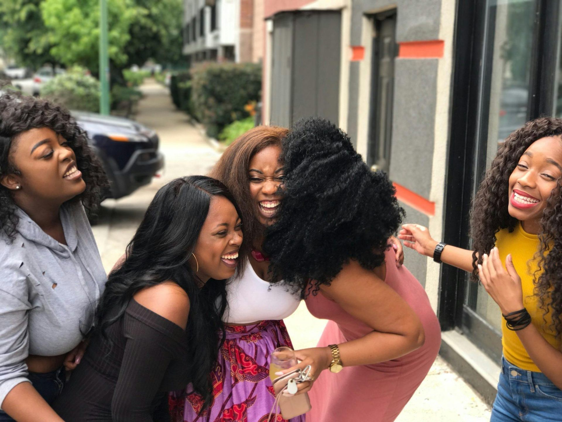 Five women laughing and embracing outdoors.