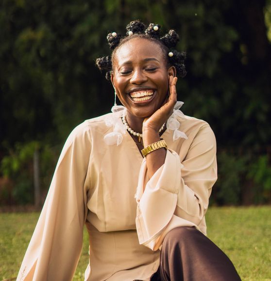 A black woman with bantu knots, smiles kindly for the camera.