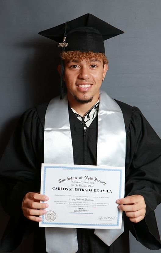 Graduate in cap and gown holding a diploma against a dark background.