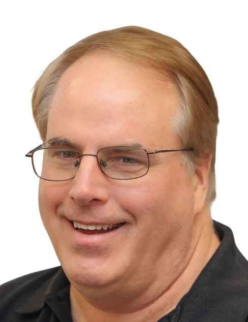 Smiling man with glasses in a black shirt against a white background