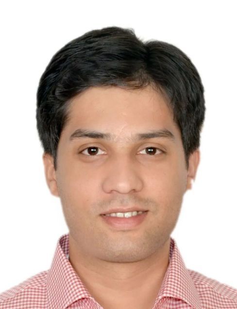 Headshot of a man with short dark hair wearing a pink checkered shirt on a white background