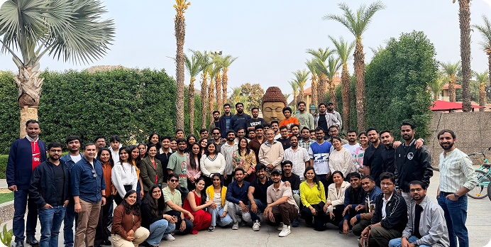 Large group posing outdoors in a garden with palm trees, arranged in rows for a group photo