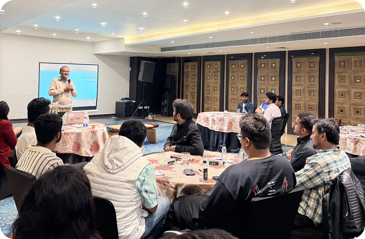 Speaker presenting to seated audience in a banquet room with round tables and a large screen at the front