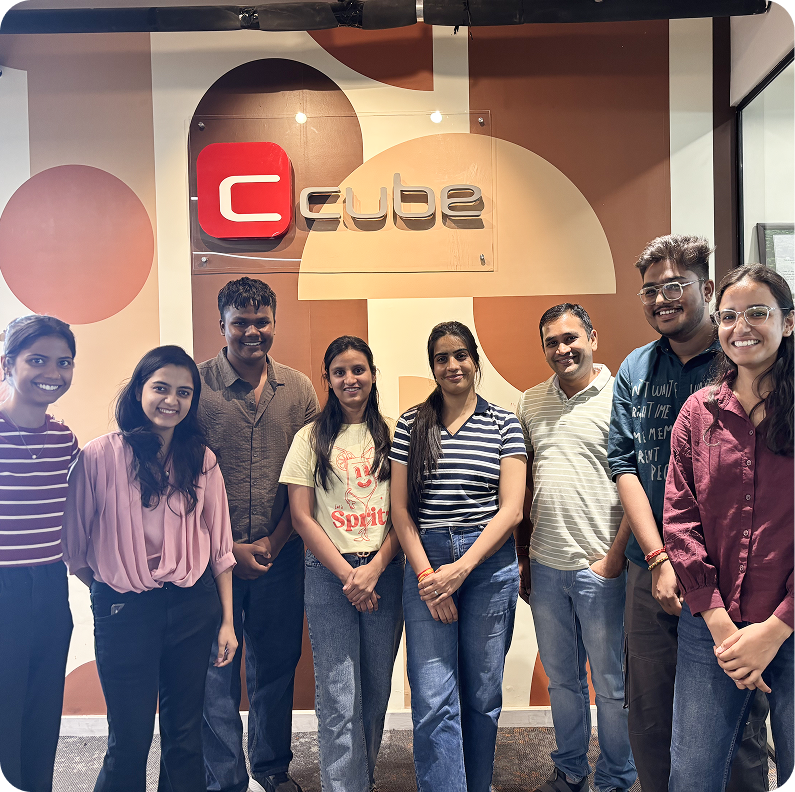 Seven people posing in front of a Cube office sign, smiling indoors.