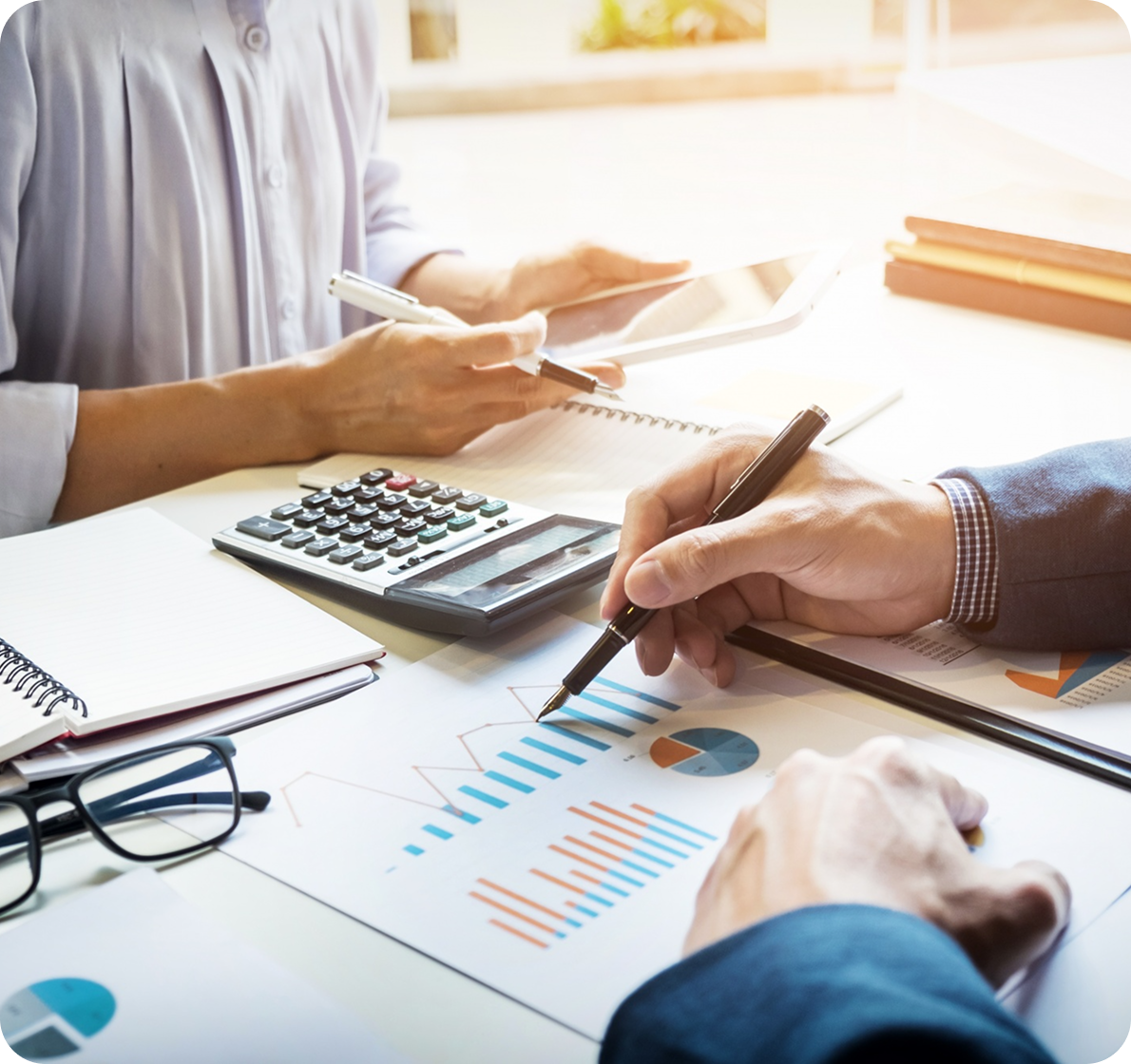 Hands discussing printed charts and graphs at a desk with calculator and glasses