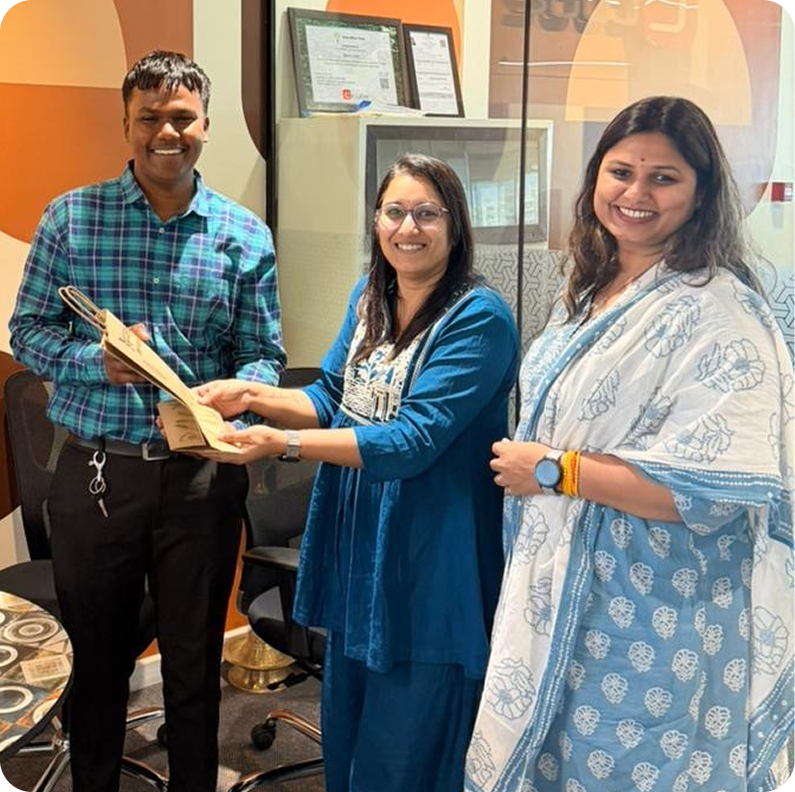 Three smiling coworkers holding a framed plaque in an office lobby