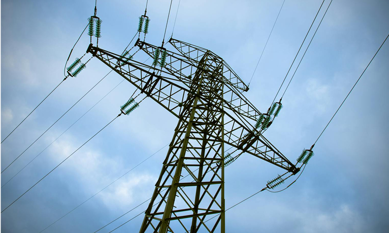 High-voltage transmission tower with power lines against a cloudy sky