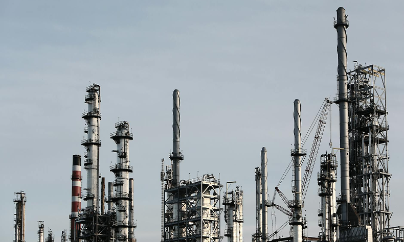 Industrial refinery with tall smokestacks and metal towers against a pale sky