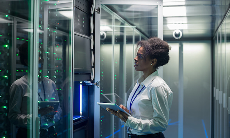 Technician using a tablet in a server room with illuminated racks and reflective glass panels