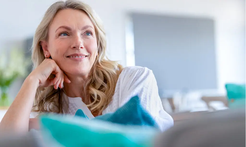 Smiling woman in a white shirt resting her chin on her hand in a bright room