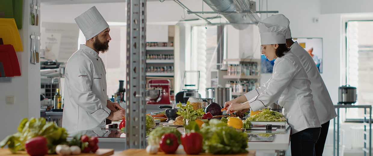 Two chefs in white uniforms preparing food in a bright commercial kitchen