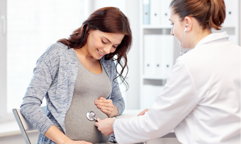 Pregnant woman smiling as doctor checks her belly in a bright clinic