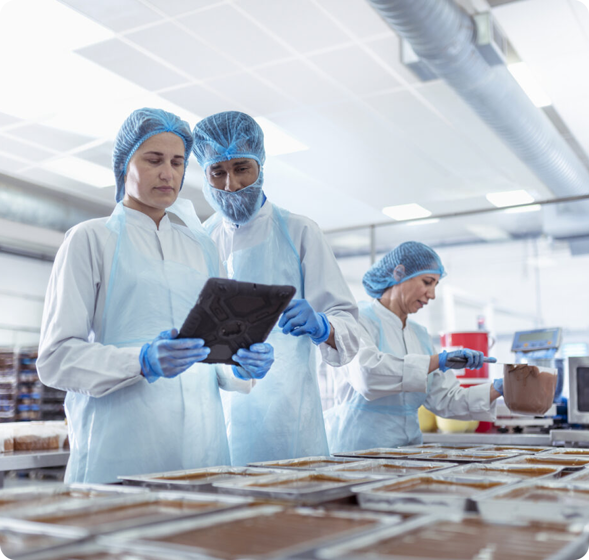 Scientists in white lab coats and blue gloves inspect samples in a bright food testing lab.