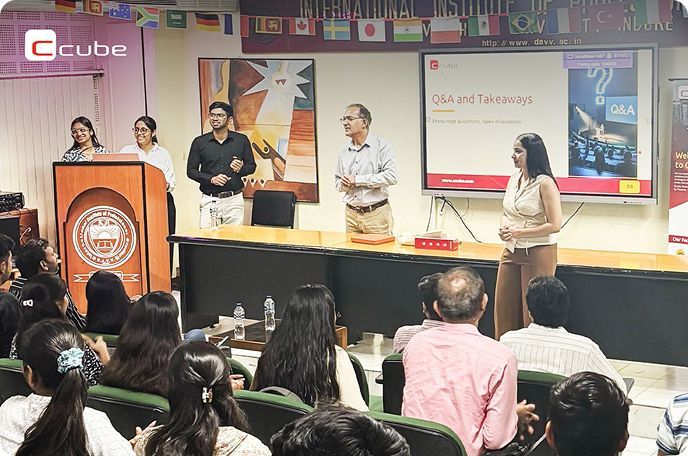 Panelists speaking at a conference in front of an audience, with a presentation screen and podium.