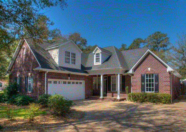 Brick house with a two-car garage, porch, and black shutters under a sunny sky.
