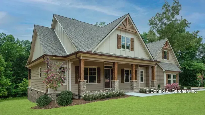 Tan Craftsman-style house with a front porch, brown shutters, and a green lawn under a blue sky.