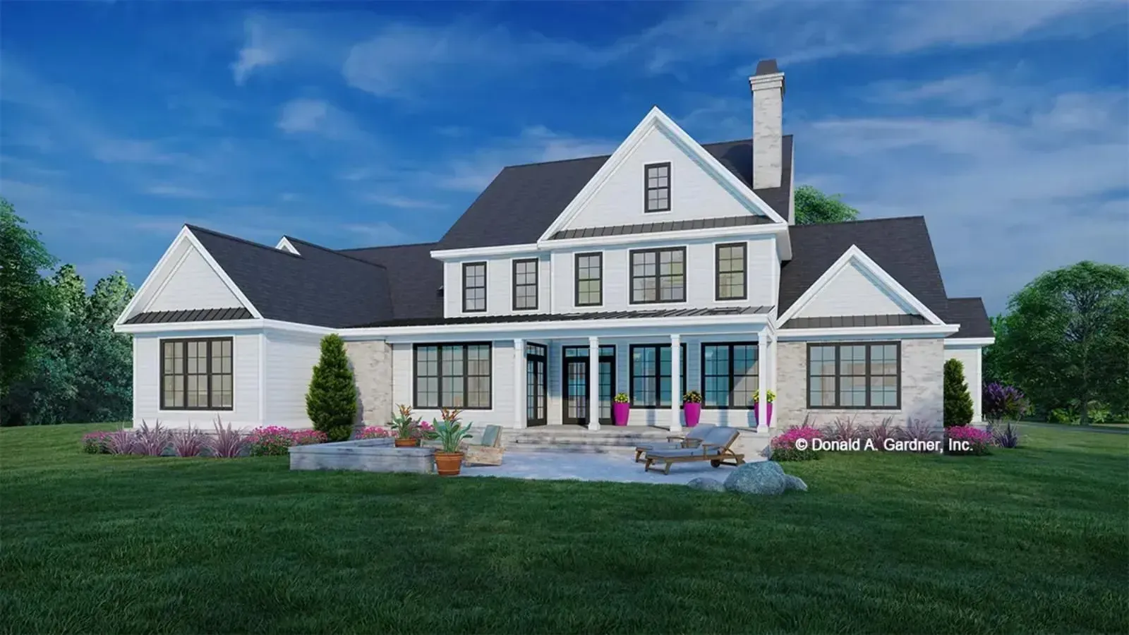 Large white farmhouse with black roof, patio, and green lawn under blue sky.