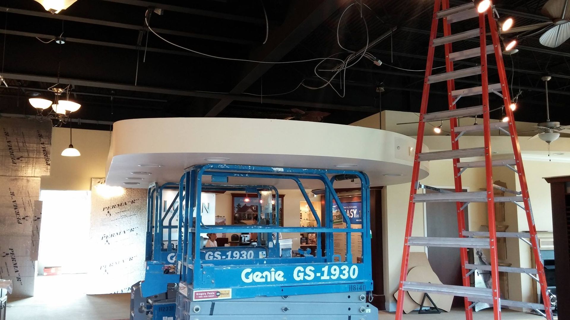 Blue Genie lift and red ladder in a room under construction with exposed ceiling wires