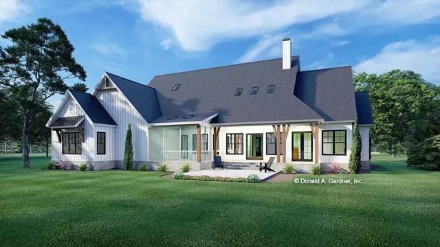 Rear view of a white farmhouse with a dark gray roof, chimney, and patio, on a grassy lawn, sunny day.