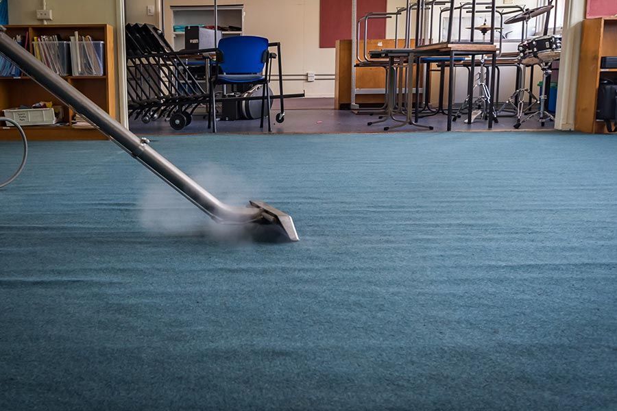 A Vacuum Cleaner is Cleaning a blue Carpet in a Classroom — Coffs Carpet Cleaning in Coffs Harbour, NSW	