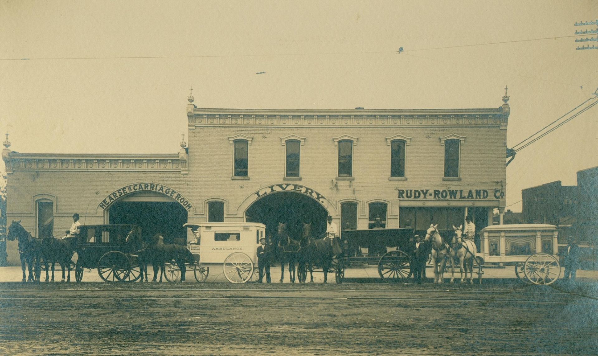Vintage sepia street scene of a two-story storefront with a horse-drawn carriage parked outside