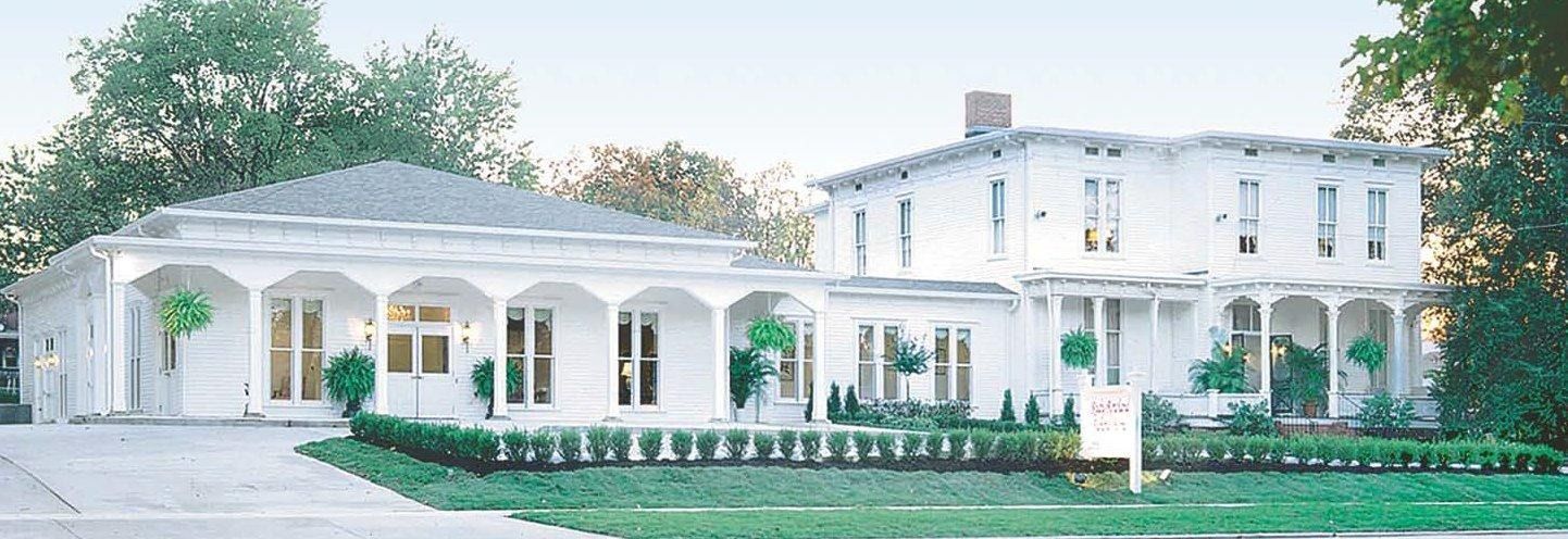 White colonial-style mansion with arched porch and landscaped lawn