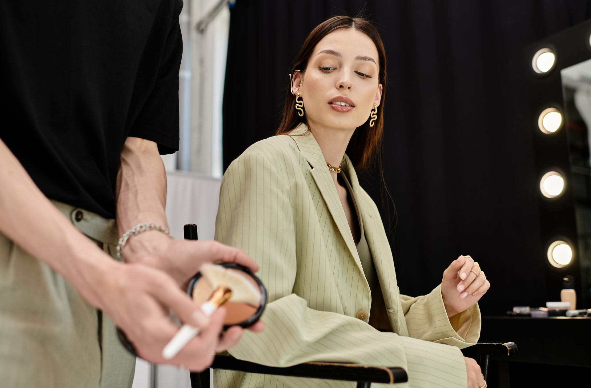 A woman is sitting in a chair while a man applies makeup to her face.