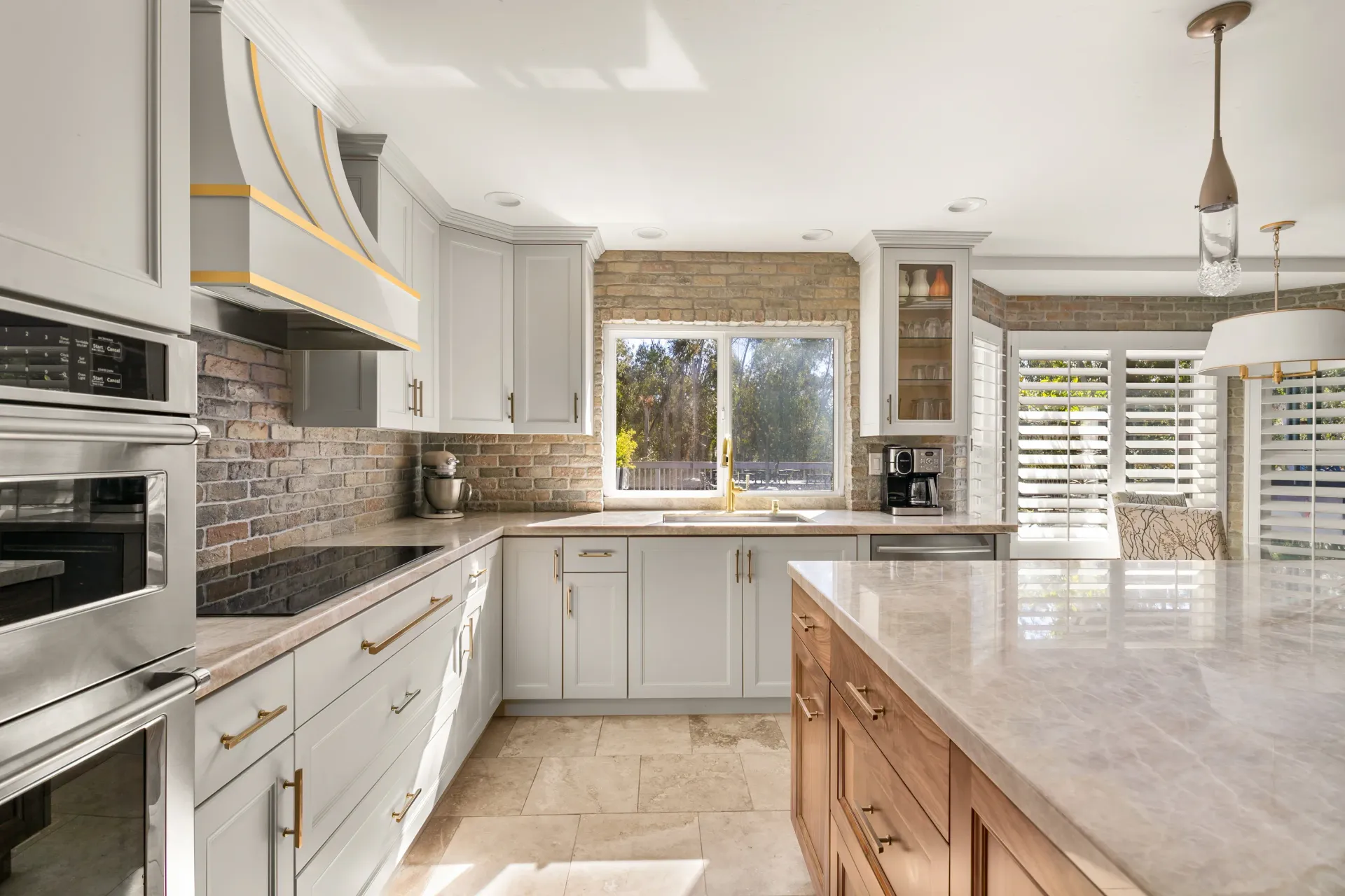 Bright modern kitchen with white cabinets, marble island, and large window with shutters