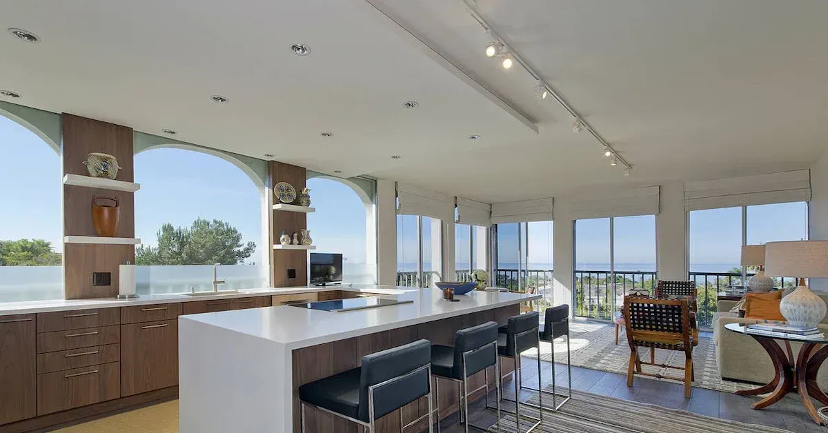 Modern open kitchen and dining area with white island, wood cabinets, and ocean-view windows