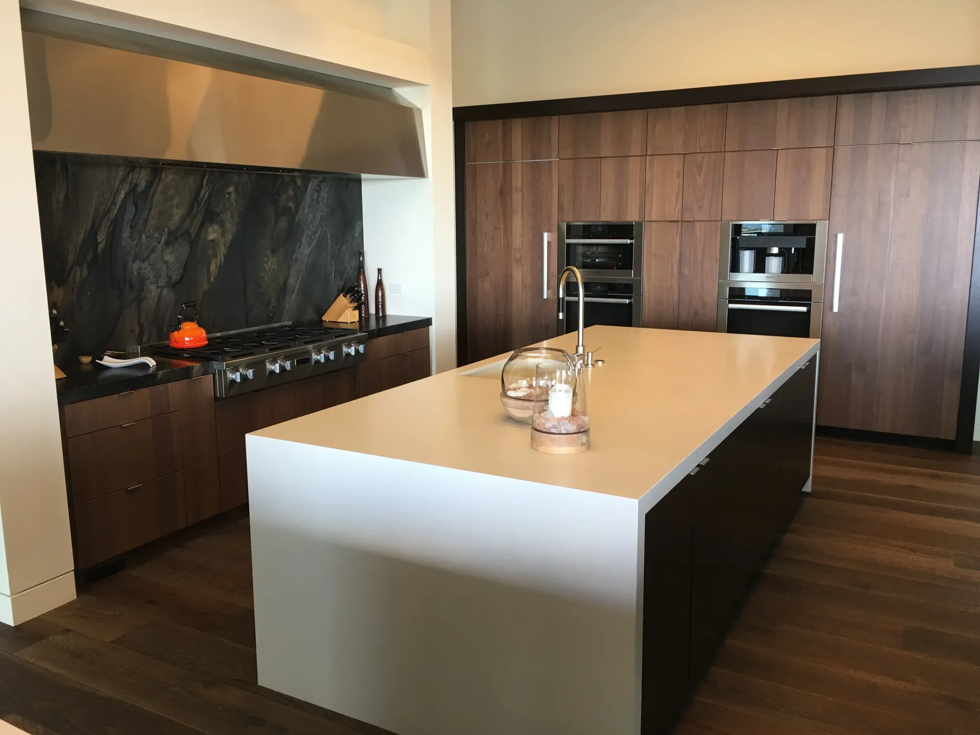 Modern kitchen with a large white island, dark wood cabinetry, and built-in ovens and fridge