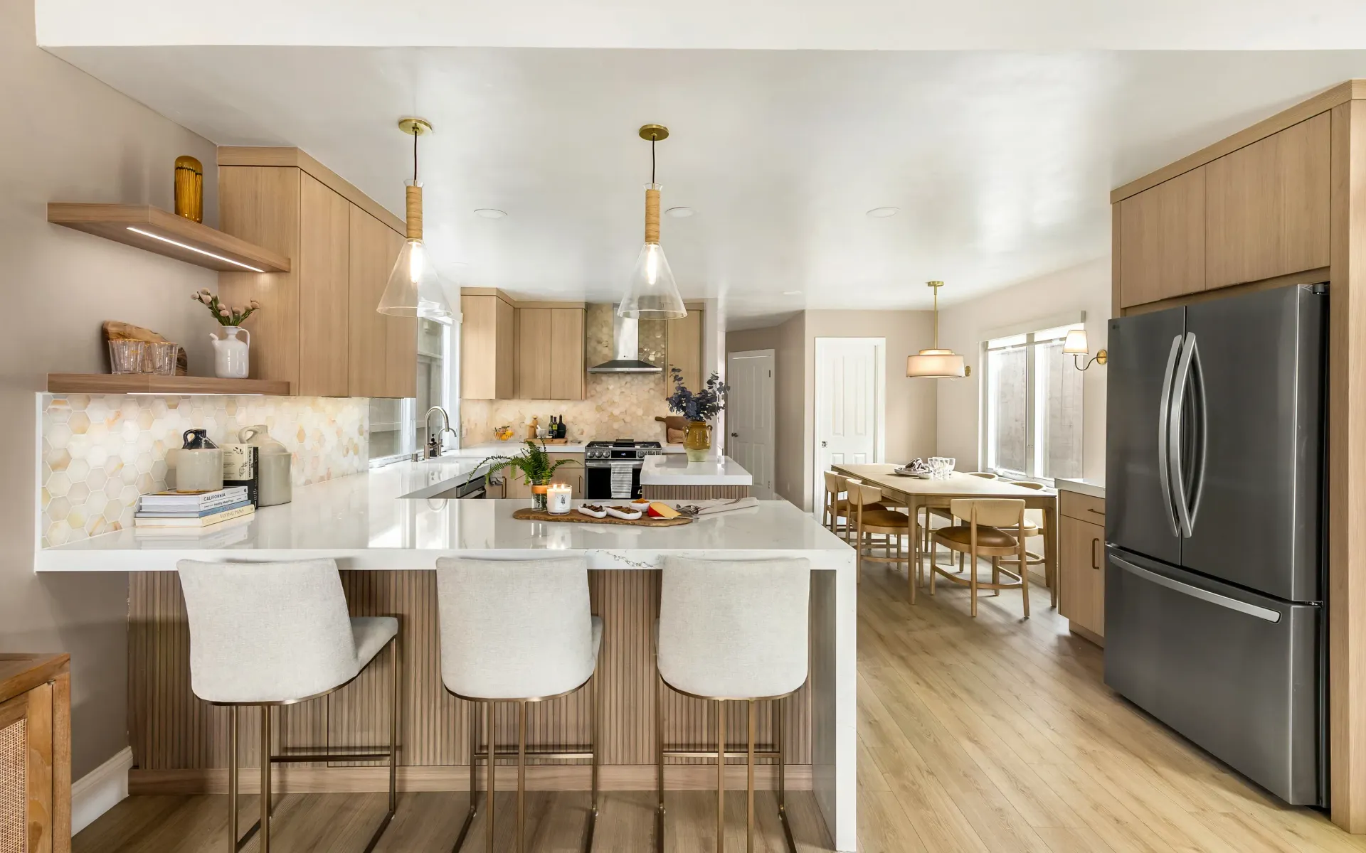 Modern kitchen with light wood cabinets, white island stools, and stainless steel refrigerator and appliances