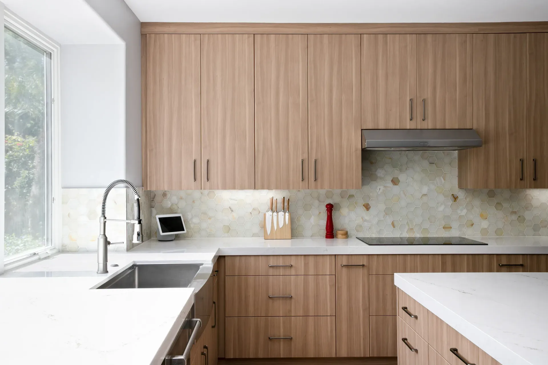 Modern kitchen with light wood cabinets, white countertops, and a large window over the sink.