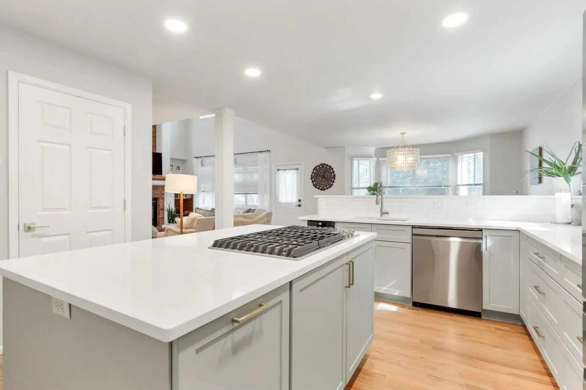 Bright modern kitchen with white cabinets, island, stainless dishwasher, and hardwood floors