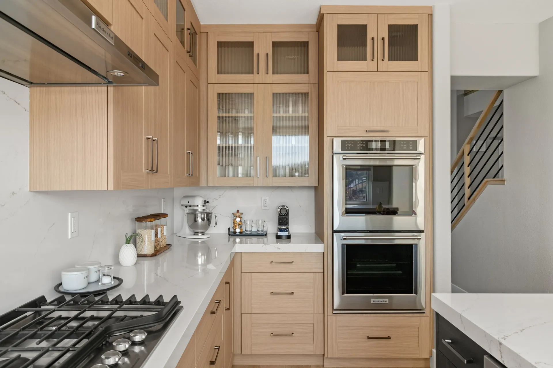 Modern kitchen with light wood cabinets, white countertops, and built-in oven and stove.