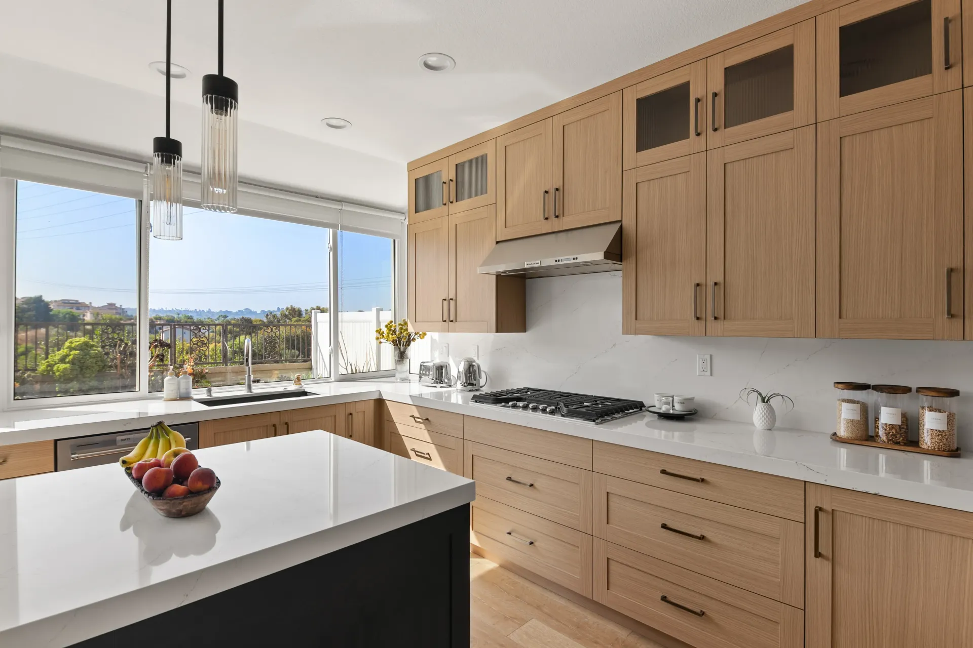 Bright modern kitchen with wood cabinets, white island, and large window overlooking a city view