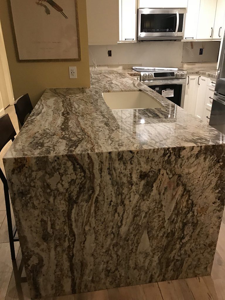 Granite kitchen island with sink and stovetop in a modern white kitchen