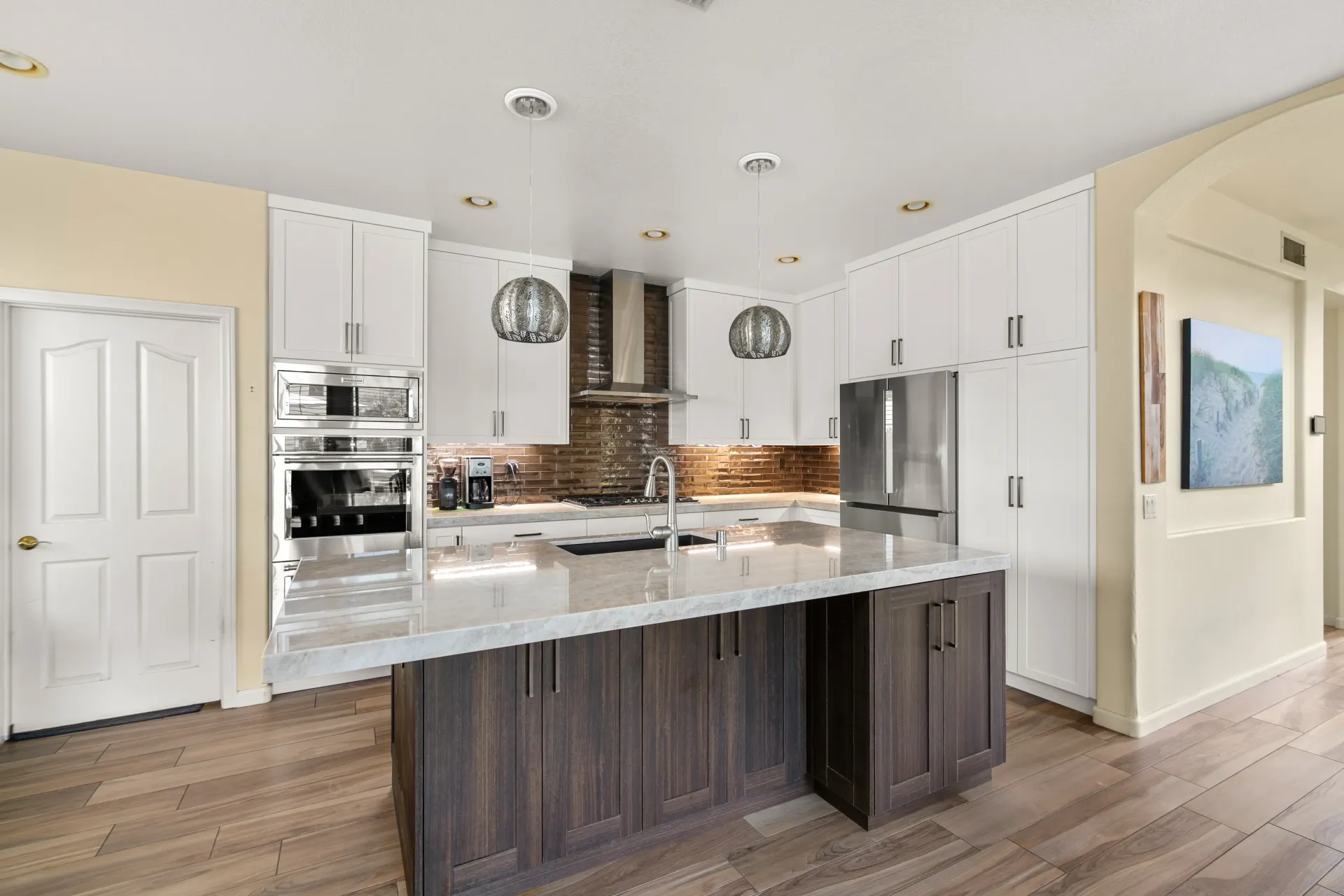 Modern kitchen with white cabinets, marble island, stainless appliances, and wood floors