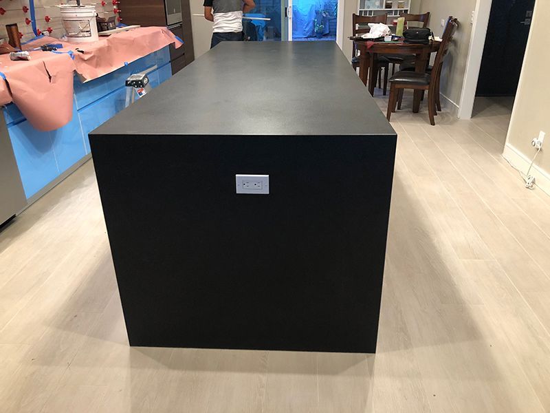 Black rectangular kitchen island in a modern open-plan room with light wood floors.