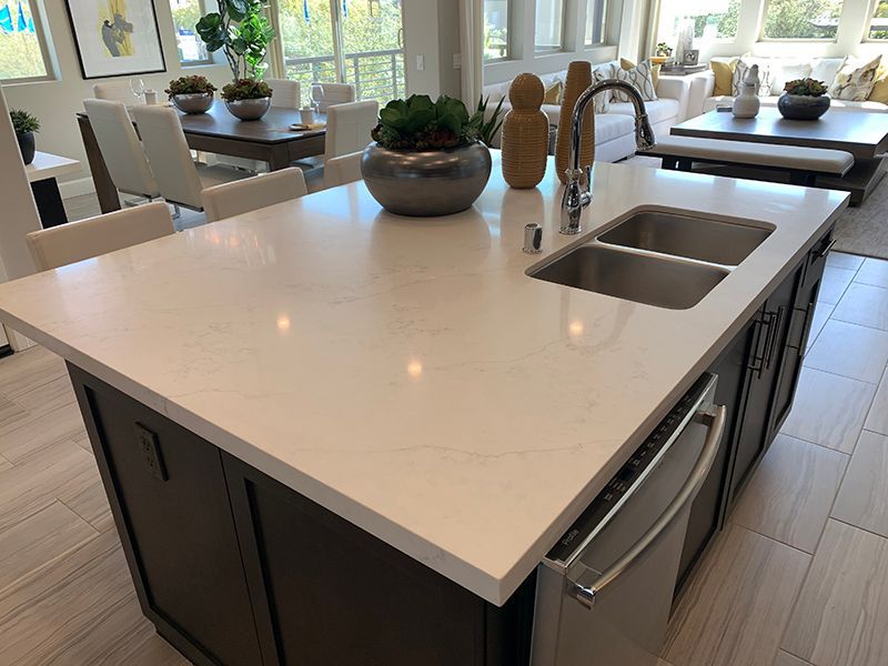 Modern kitchen island with white countertop, double sink, and dining area in the background