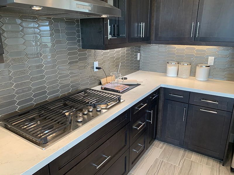 Modern kitchen with dark cabinets, white countertops, stainless gas range, and gray hex tile backsplash