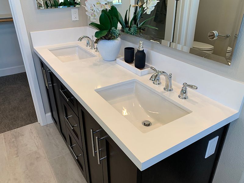 Modern bathroom vanity with double sinks, white countertop, dark cabinets, and a mirror above.