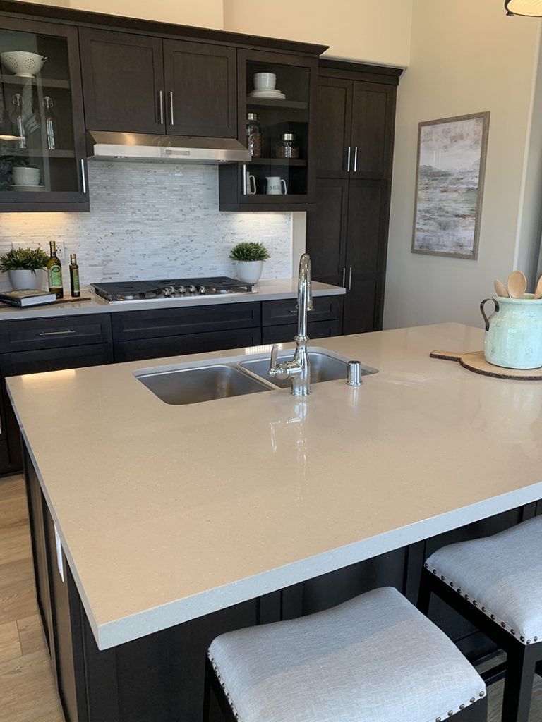 Modern kitchen with large white island, dark cabinets, stainless sink, and two stools