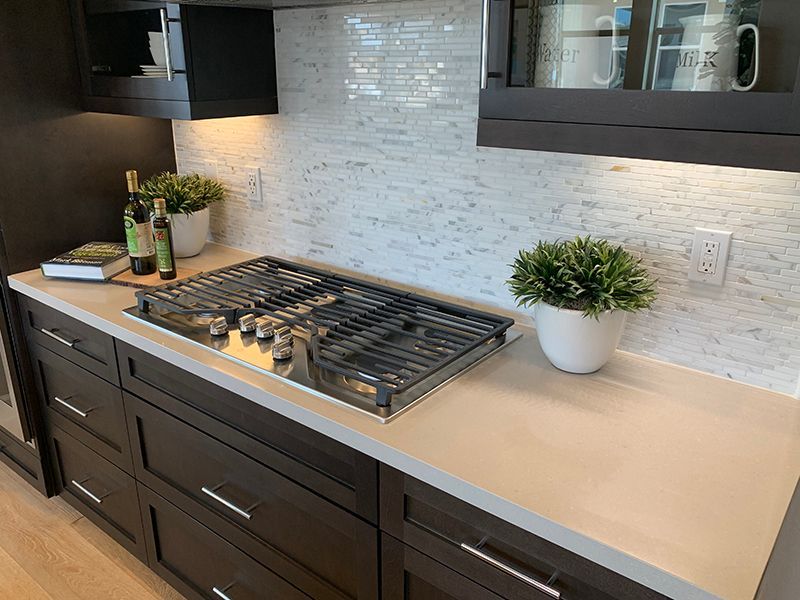 Modern kitchen countertop with gas cooktop, dark cabinets, white backsplash, and small potted plant and bottles