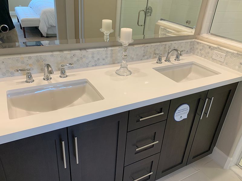 Double-sink bathroom vanity with white countertop, dark cabinets, and a mirror above.